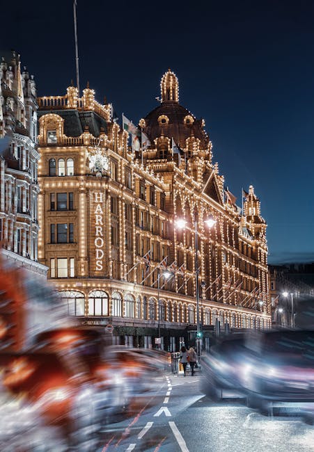 A city street scene in London showing historic architecture with ornate brick facades and a large domed building in the background. In the foreground, a double-decker bus with a digital route display 